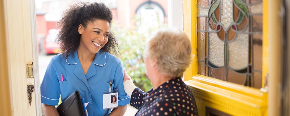 Home-Nurse-Picture - Seasons Hospice MO | End of Life Care | Springfield, MO A nurse visits her patient at home and smiles as she's welcomed through the door.