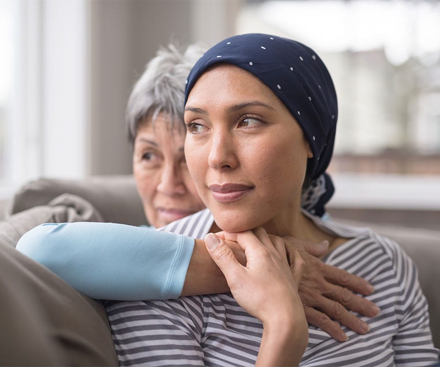 A younger patient and older family member sit holding each other, gazing outward through a window together.