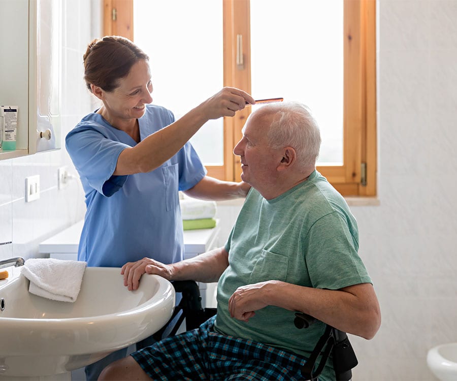 A happy looking man gets his hair combed by a care team member who engages in conversation with him.